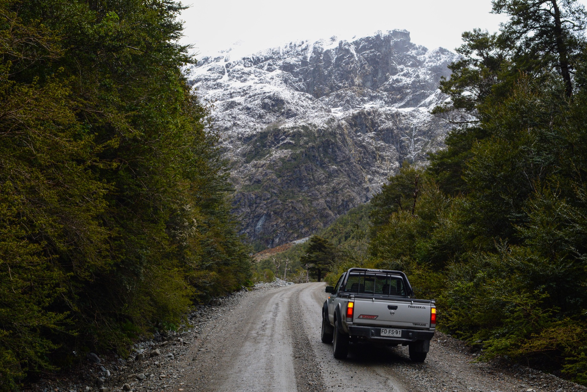 A gravel Carretera Austral road beside forest and snow-covered mountains