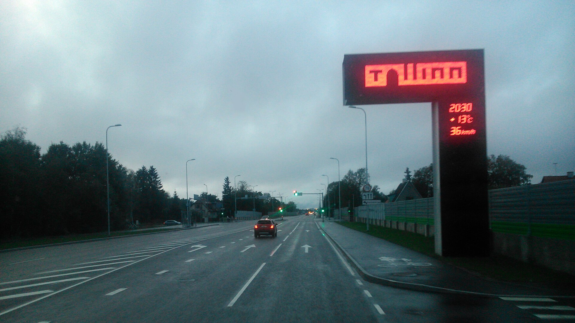 Wet multi-lane road approaching Tallinn with the city entrance sign and traffic lights ahead
