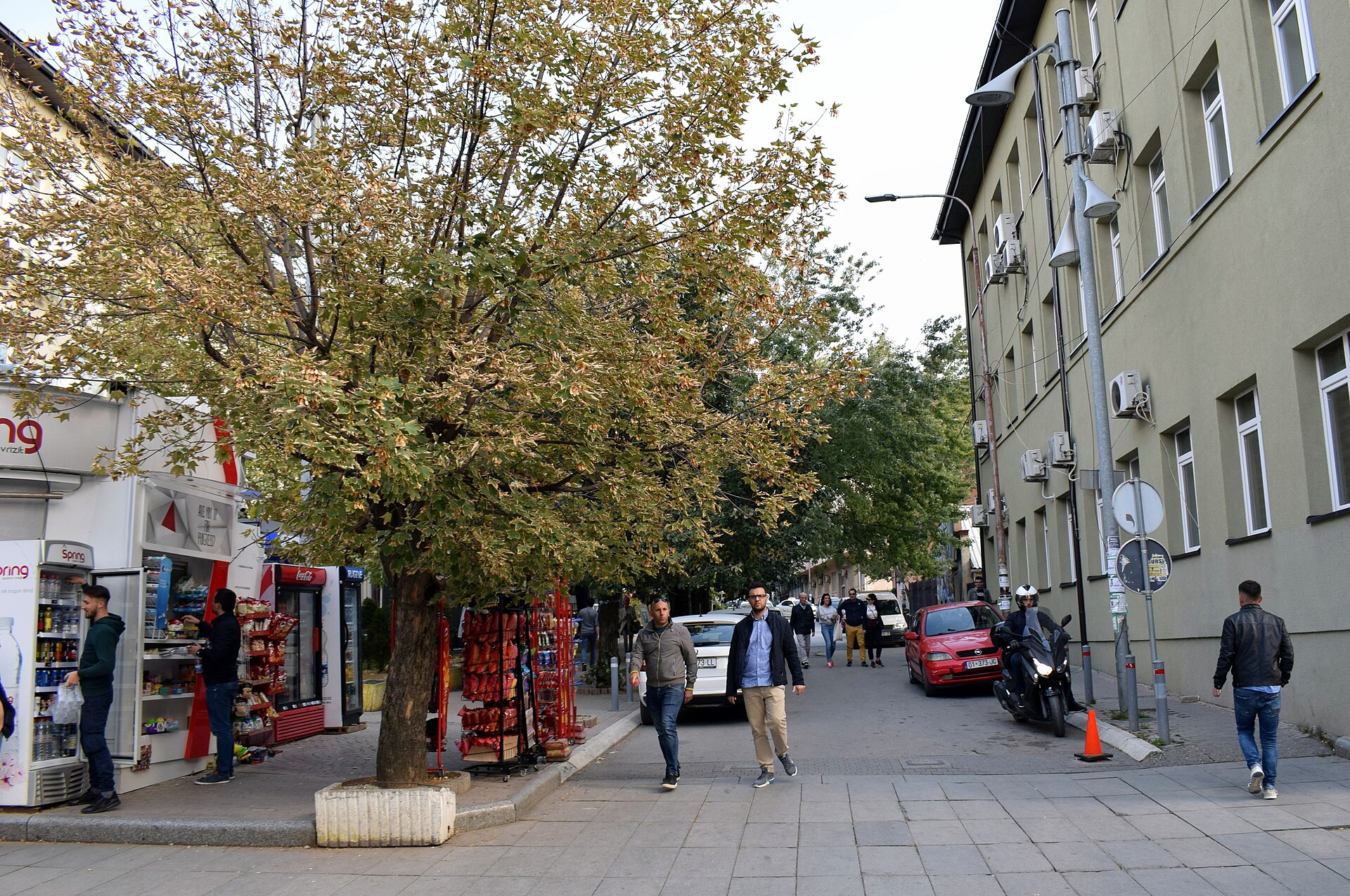 A busy street scene in Prishtina with cars, pedestrians and parking signs