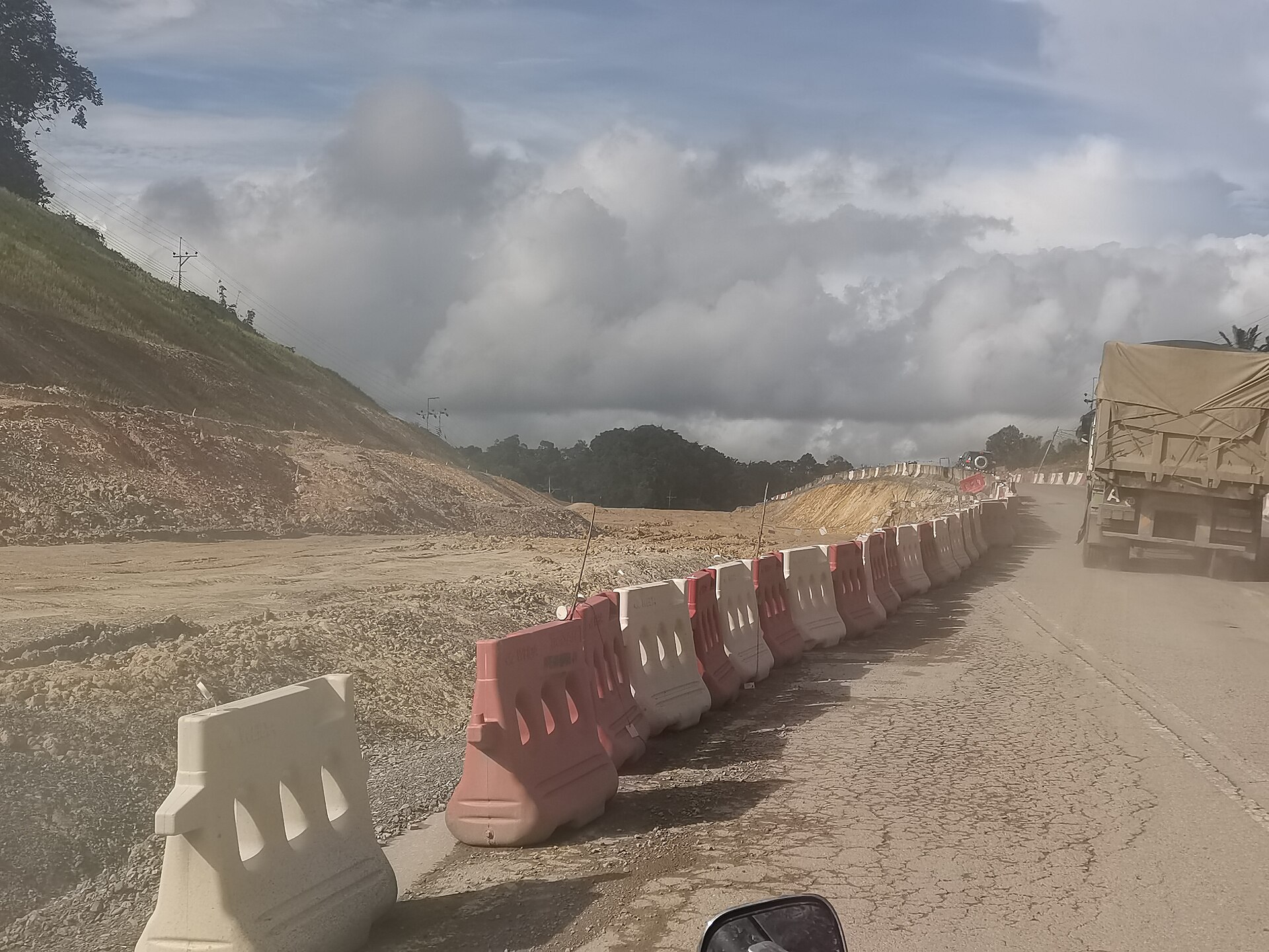 Pan-Borneo Highway work zone near Sebangkoi Park in Sarawak with trucks and temporary barriers
