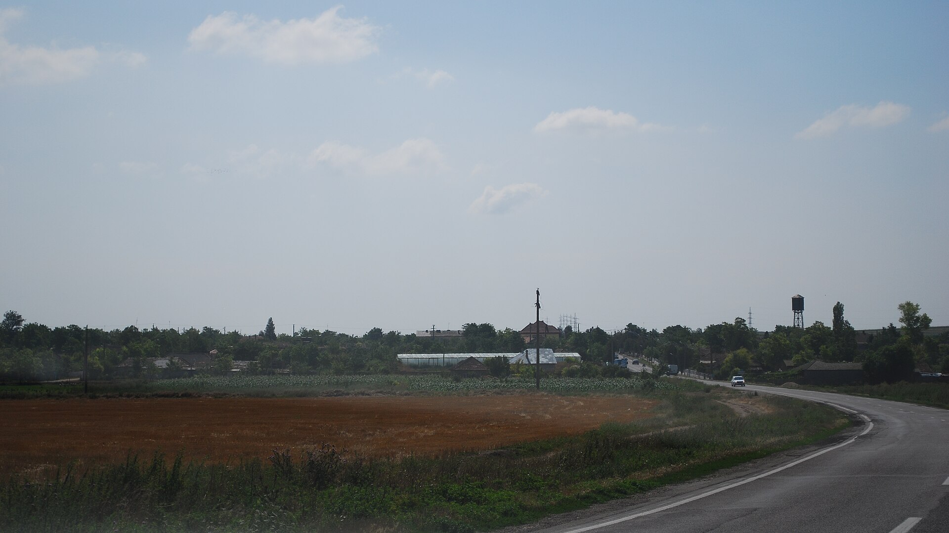 A two-lane road approaching a Romanian village beside fields