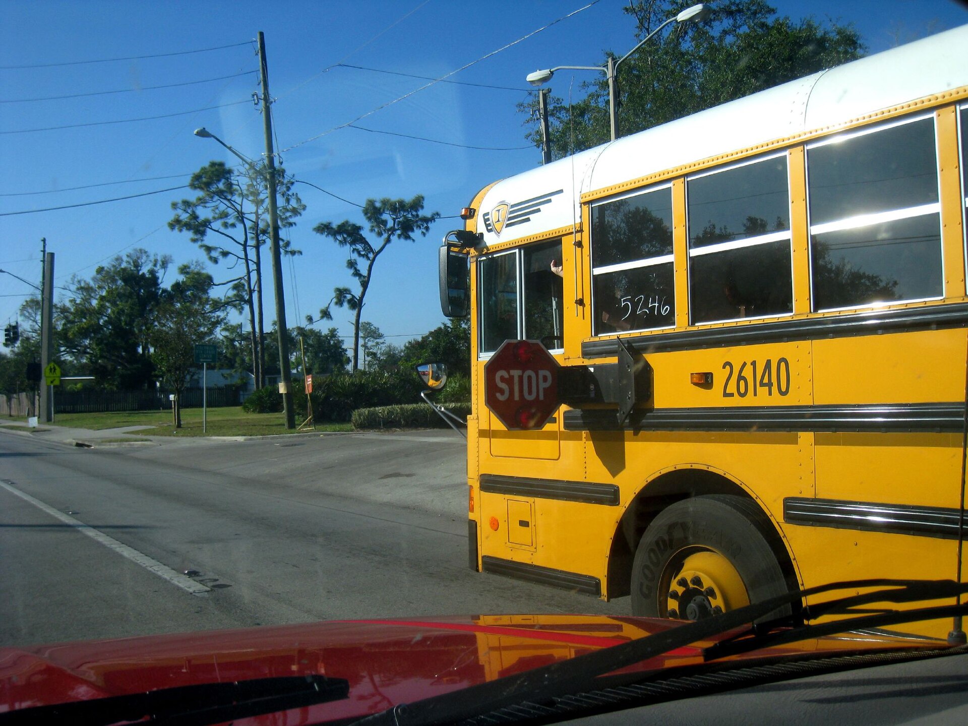 Yellow US school bus with its red stop arm extended at a neighborhood crossing